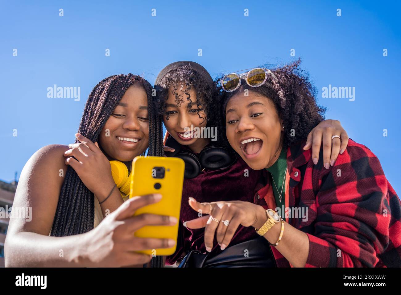 Vue en angle bas de trois amis multi-ethniques souriant tout en partageant un mobile en plein air Banque D'Images