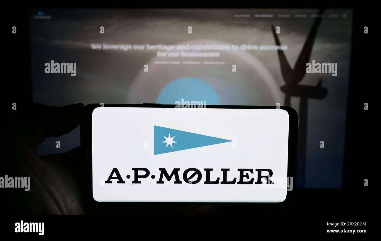 Personne tenant un téléphone portable avec le logo de la société danoise A.P. Moller Holding AS (APMH) sur l'écran devant la page Web. Concentrez-vous sur l'affichage du téléphone. Banque D'Images