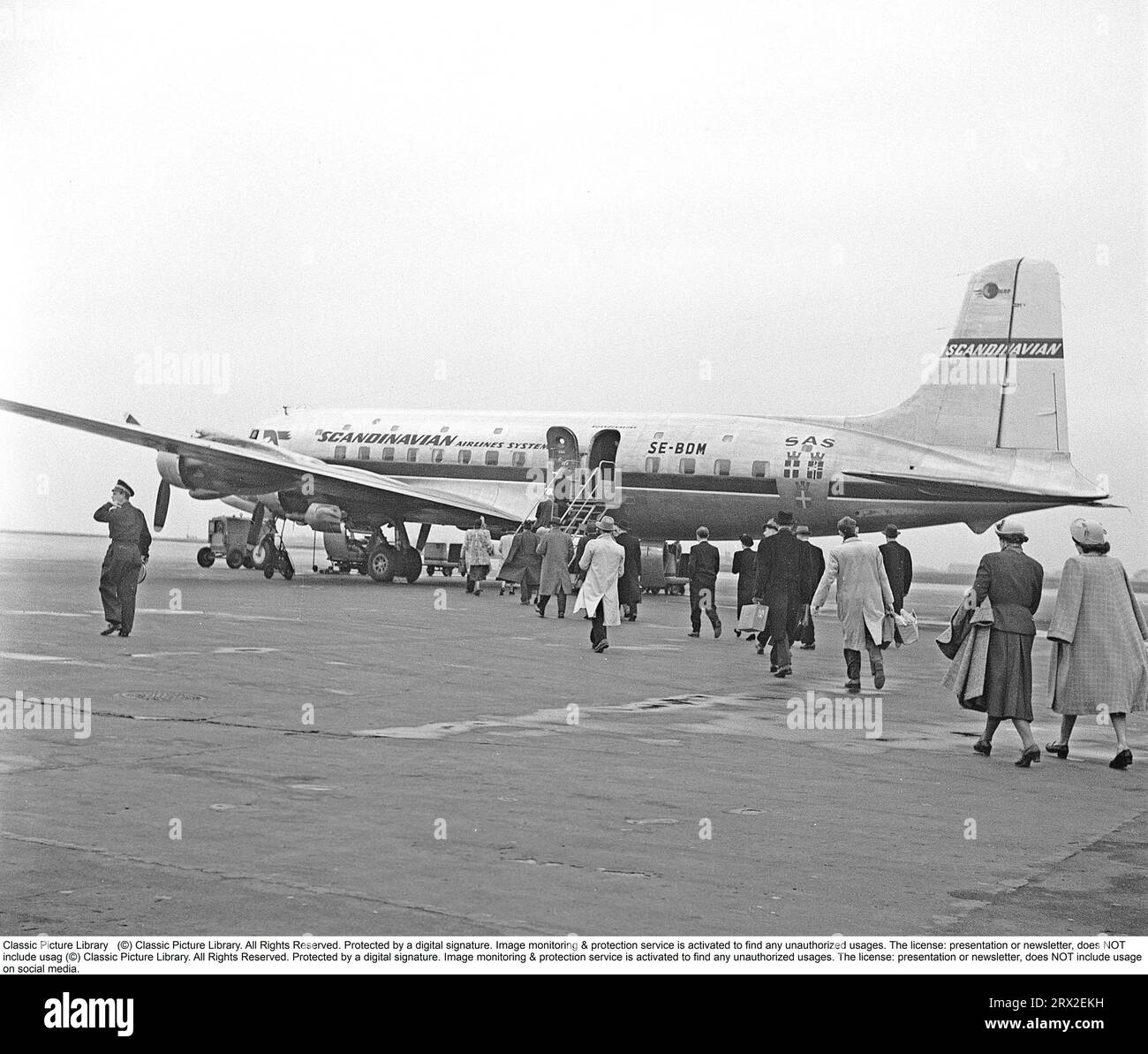 Passagers aériens dans les années 1950 Un avion de passagers quadrimoteur de type se-BDM Douglas DC-6-477B Cloudmaster de la compagnie aérienne scandinave SAS est aligné dans un aéroport suédois et les passagers aériens ont commencé à monter les escaliers et à monter à bord de l'avion. Le temps est un peu gris et terne et on peut spéculer que les Suédois qui ont commencé à voyager sur des voyages charter vers le sud de l'Europe peuvent être sur leur chemin vers où il fait chaud et ensoleillé et ainsi éviter le temps morne. Suède 1952. Kristoffersson réf. BG60-4 Banque D'Images