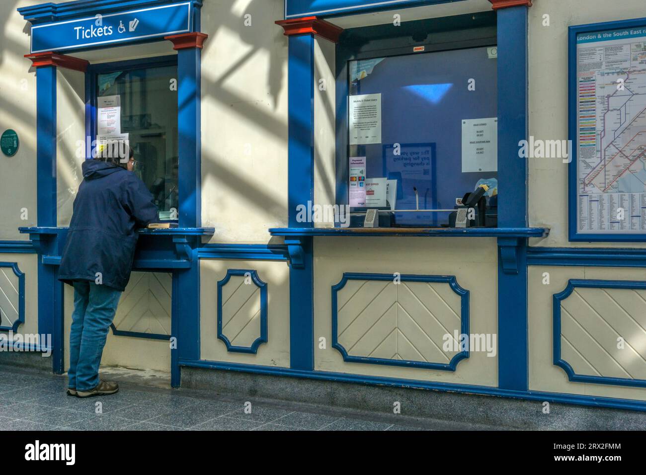 Femme achetant des billets de train ou faisant une demande à la billetterie de la gare de King's Lynn. Banque D'Images