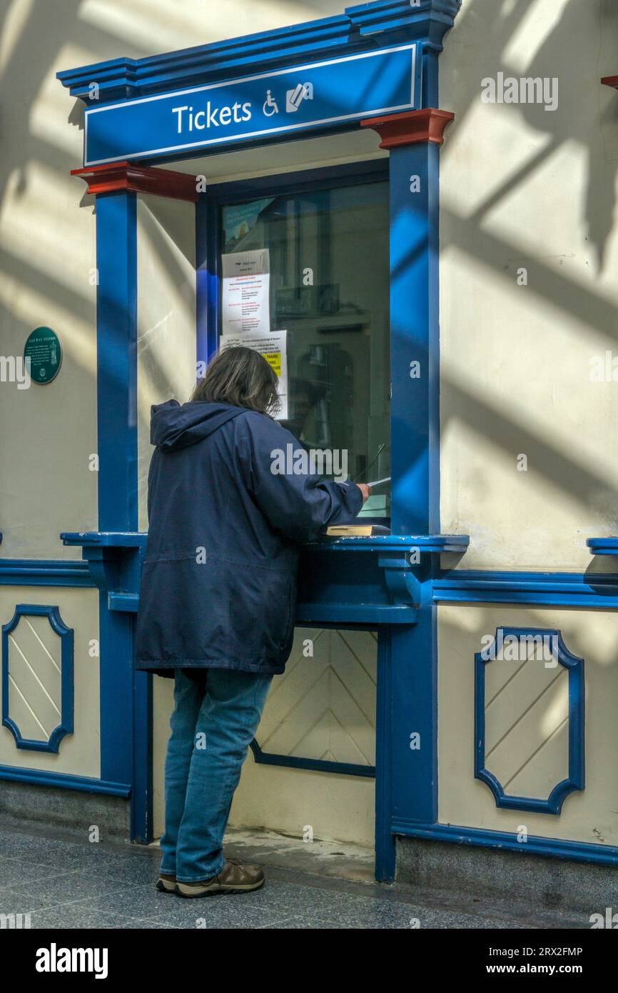 Femme achetant des billets de train ou faisant une demande à la billetterie de la gare de King's Lynn. Banque D'Images