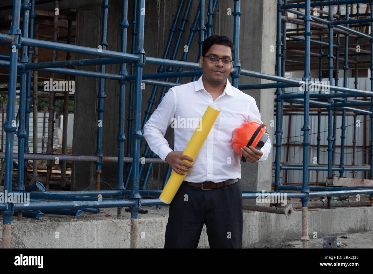 Ingénieur masculin indien ou architecte portant des vêtements formalwear tenant le plan et le casque dur sur le site de construction Banque D'Images