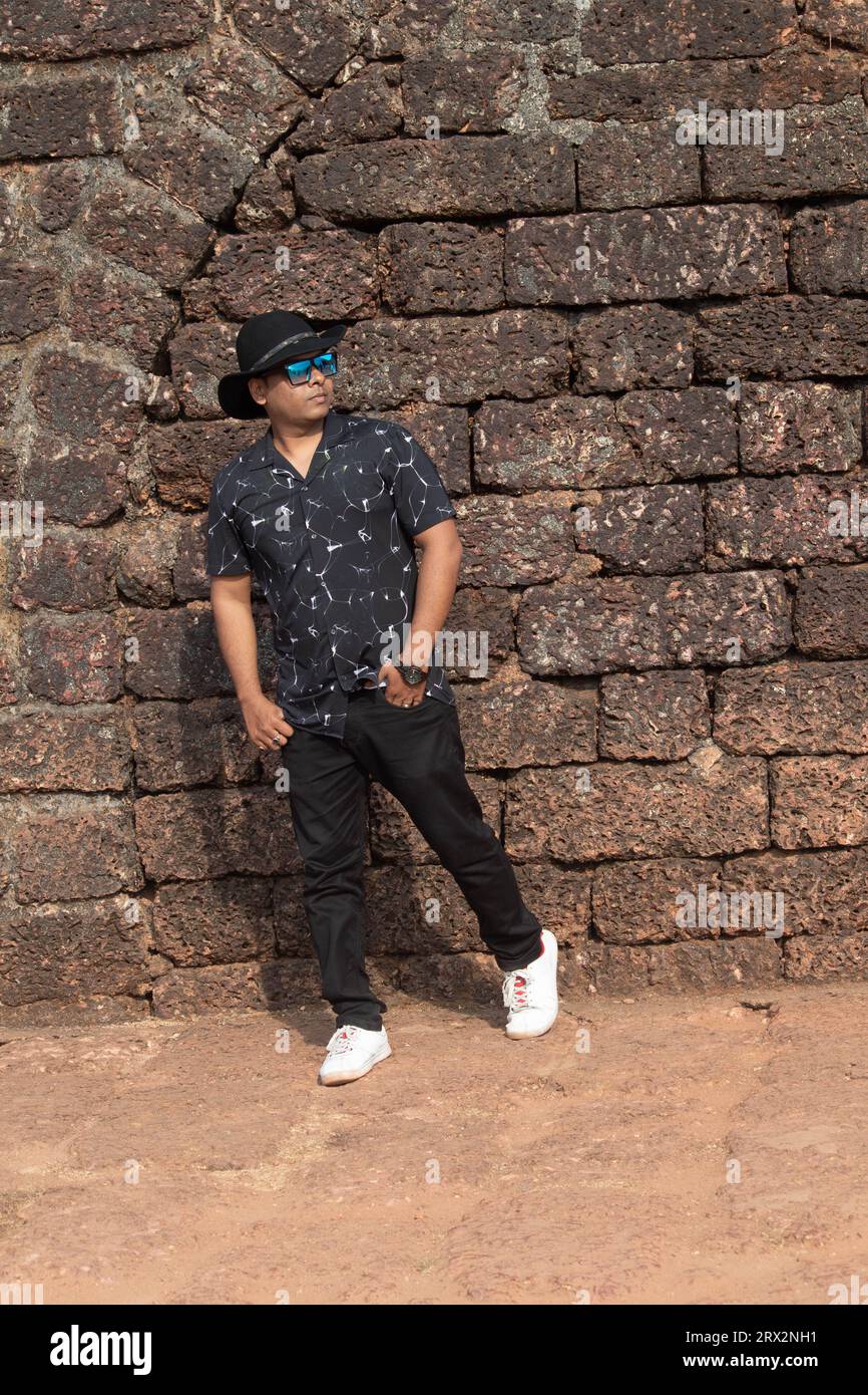 Bel homme dans le chapeau de cow-boy posingcontre mur de pierre antique. Voyageur masculin élégant dans le chapeau d'été et lunettes de soleil sur le site historique Banque D'Images
