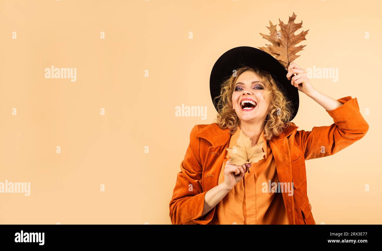 Humeur automnale. Femme heureuse en chapeau noir avec des feuilles d'automne. Modèle féminin de mode en chemise et manteau orange. Vêtements d'automne tendance. Shopping d'automne Banque D'Images