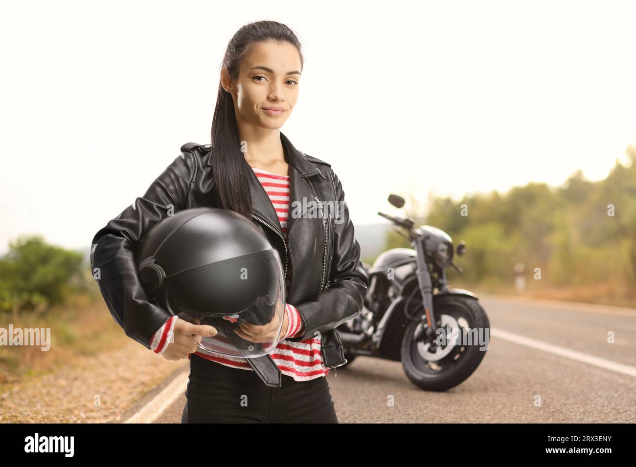 Jeune motard femelle avec un hachoir tenant un casque sur une route ouverte Banque D'Images