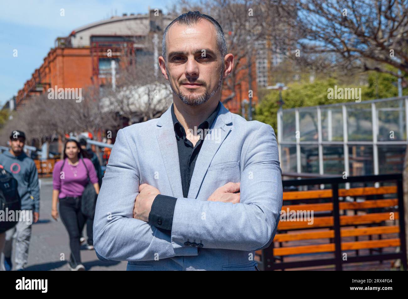 Portrait d'homme d'affaires adulte caucasien, français avec les bras croisés portant une veste élégante, debout à l'extérieur regardant la caméra souriant légèrement à mi-chemin Banque D'Images