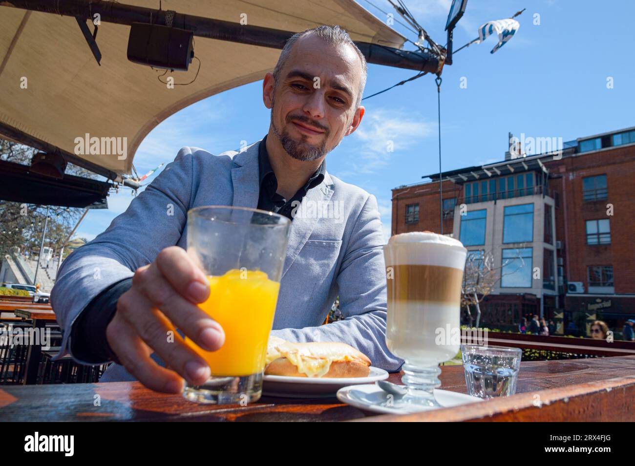 Homme d'affaires caucasien adulte français, tenant un verre avec du jus d'orange pendant le petit déjeuner, à l'extérieur au bar restaurant à Puerto Madero Argentine Banque D'Images
