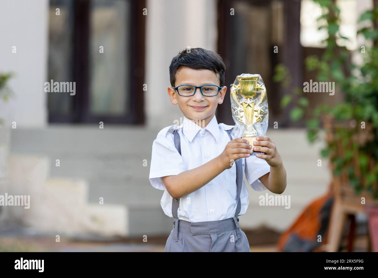 Heureux écolier indien portant l'uniforme scolaire tenant le trophée de victoire en main à l'extérieur de l'école. Concept d'éducation. Banque D'Images