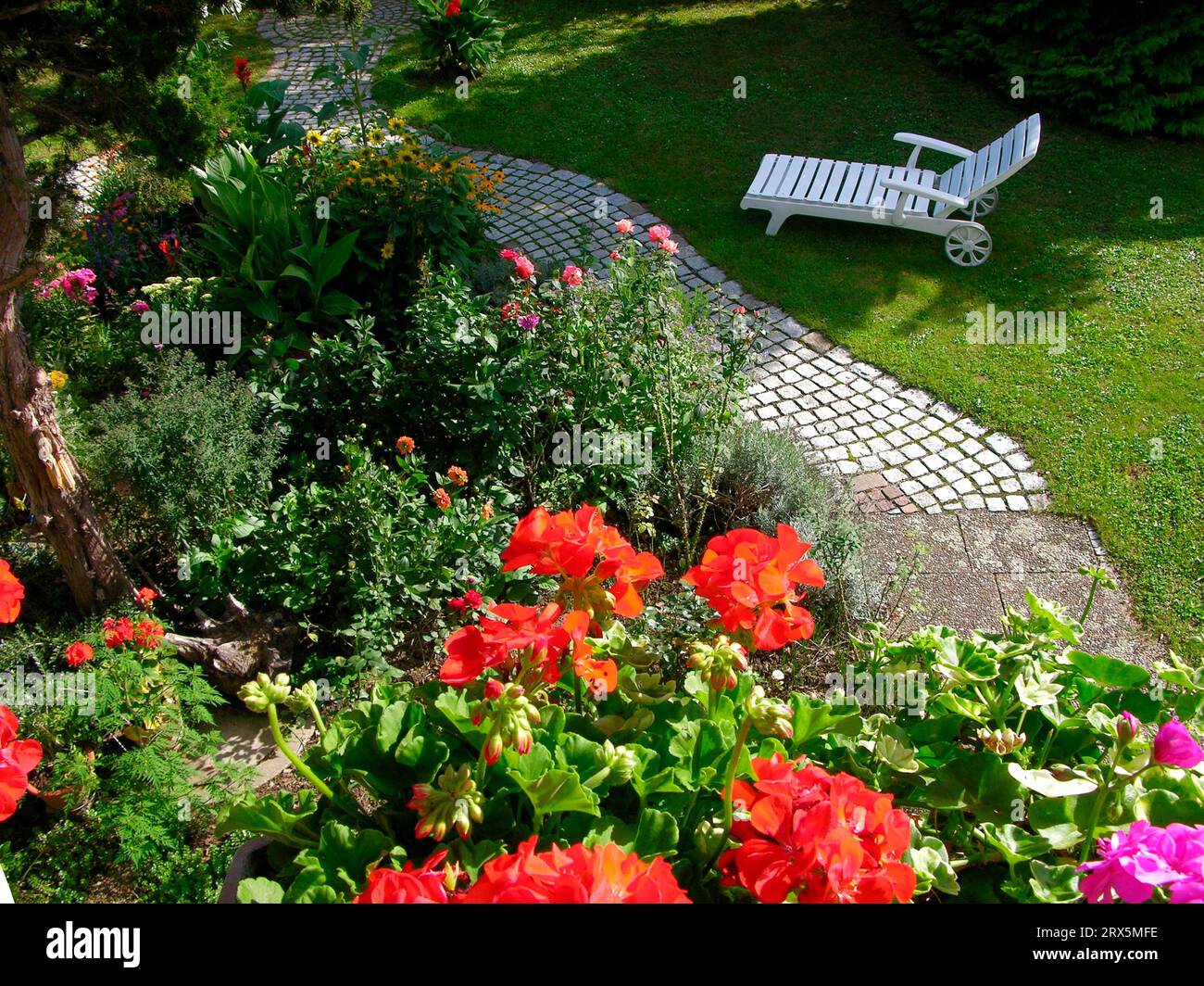 Chaise longue dans le jardin, jardin vivace avec chemin pavé, pierres, jardin d'été, jardin fleuri Banque D'Images