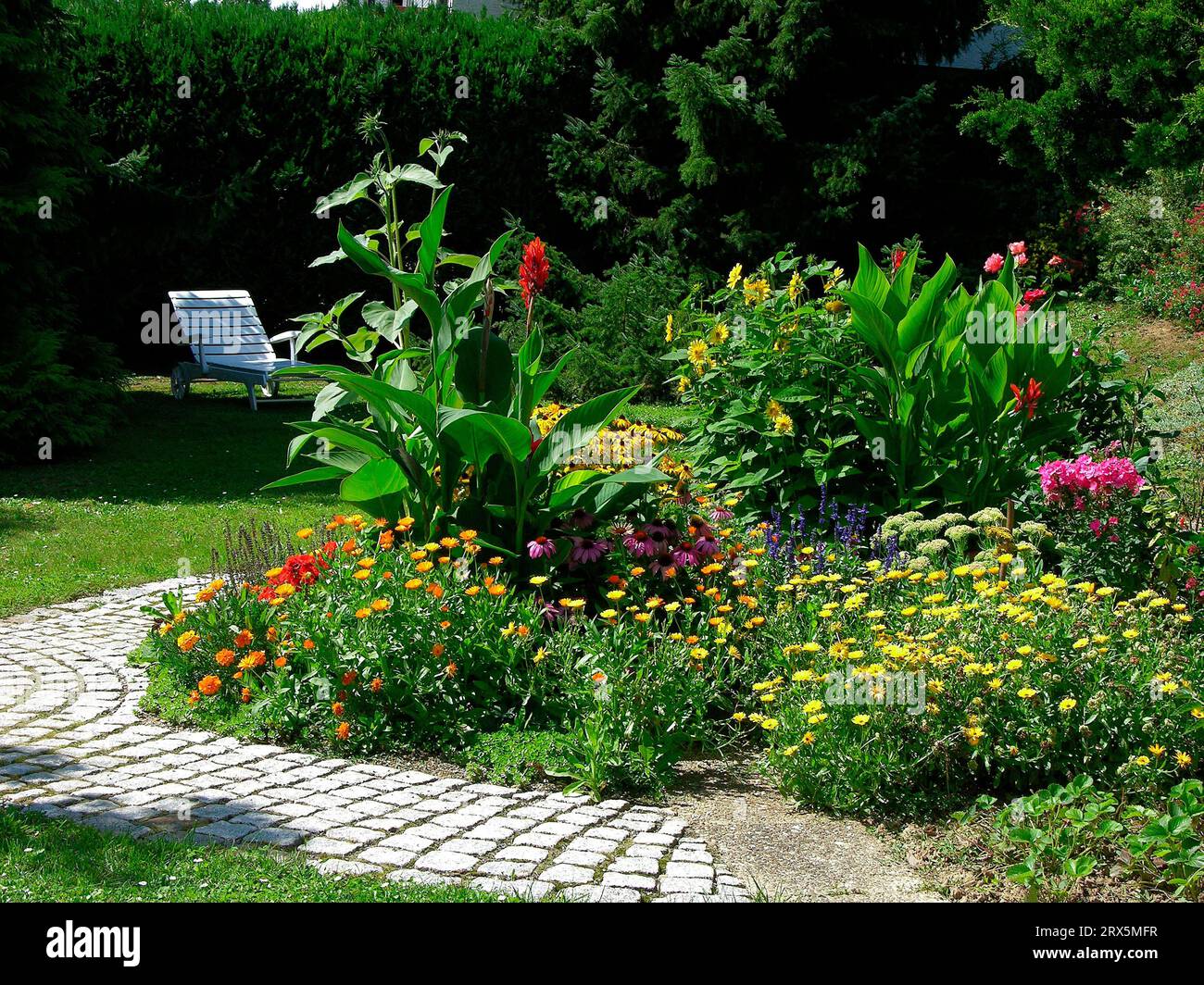 Chaise longue dans le jardin, jardin vivace avec chemin pavé, pierres, jardin d'été, jardin fleuri - Banque D'Images