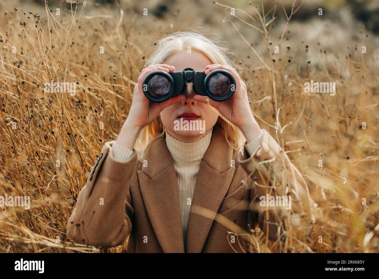 Femme blonde regardant à travers des jumelles dans le champ Banque D'Images