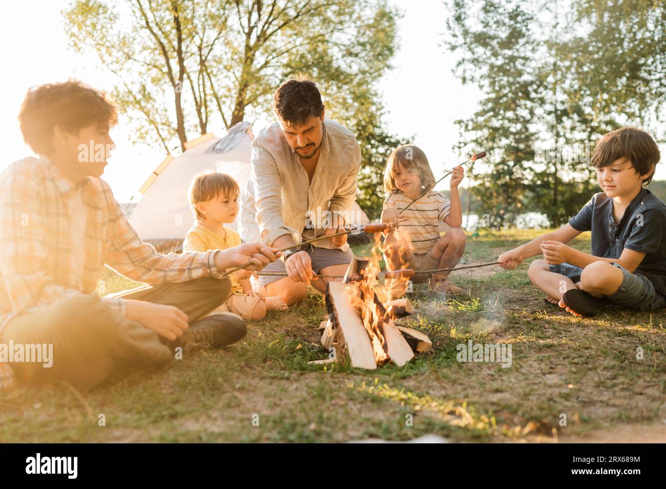 Père et enfants rôtir des saucisses ensemble au feu de joie au pique-nique Banque D'Images