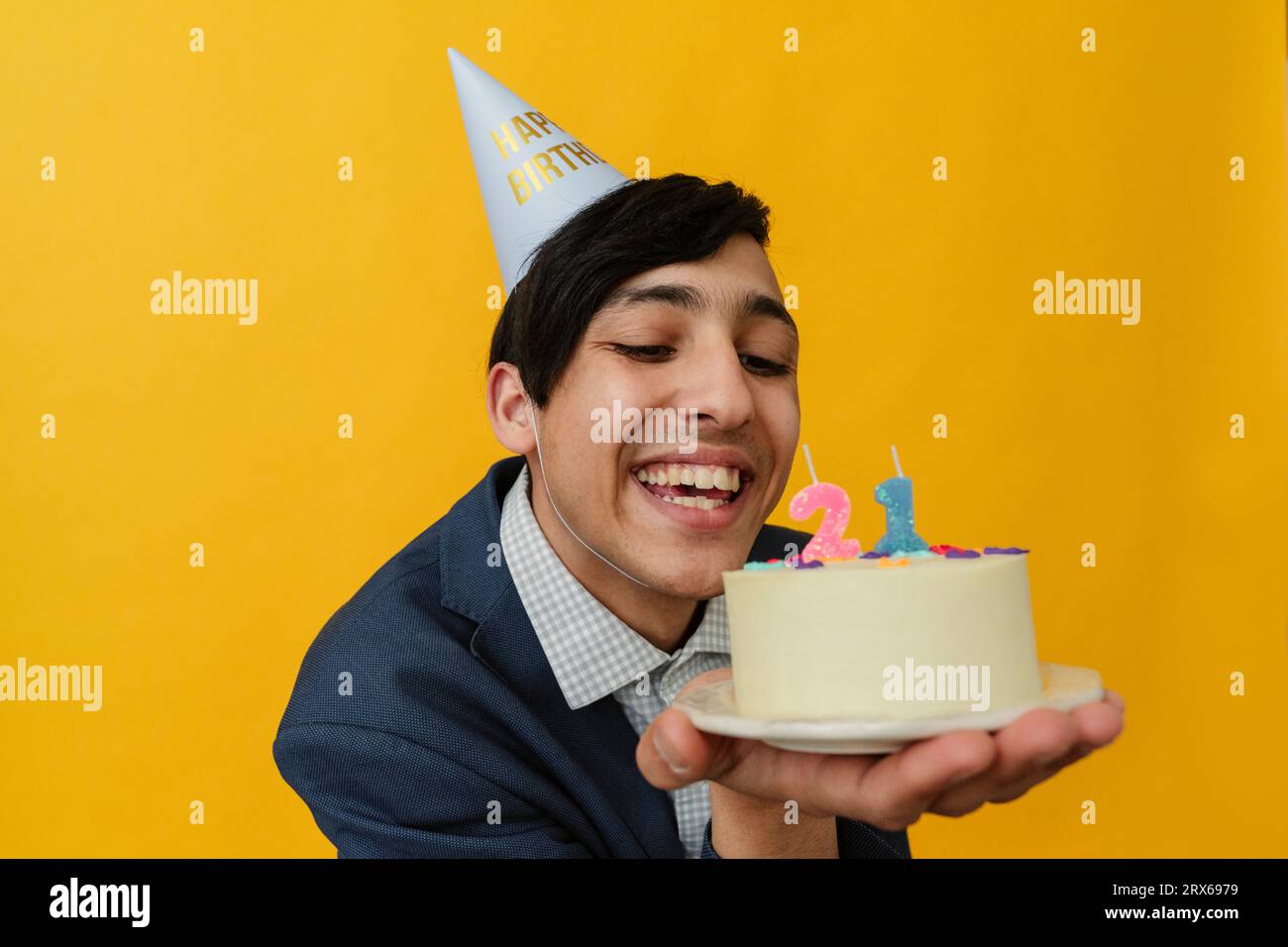 Joyeux jeune homme avec chapeau de fête regardant le gâteau d'anniversaire Banque D'Images