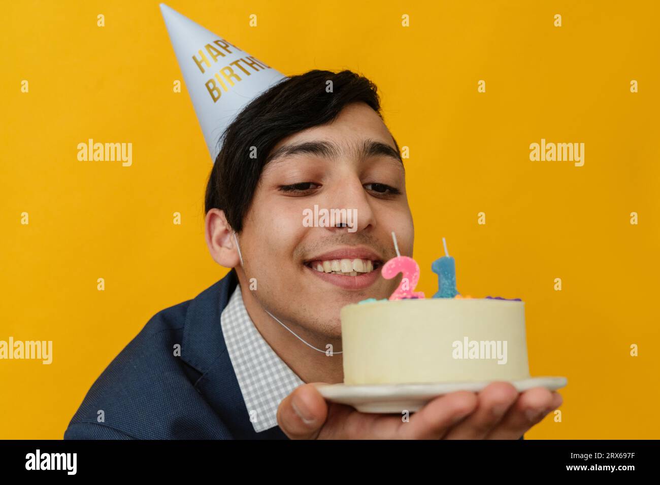 Homme heureux avec chapeau de fête regardant le gâteau de 21e anniversaire Banque D'Images