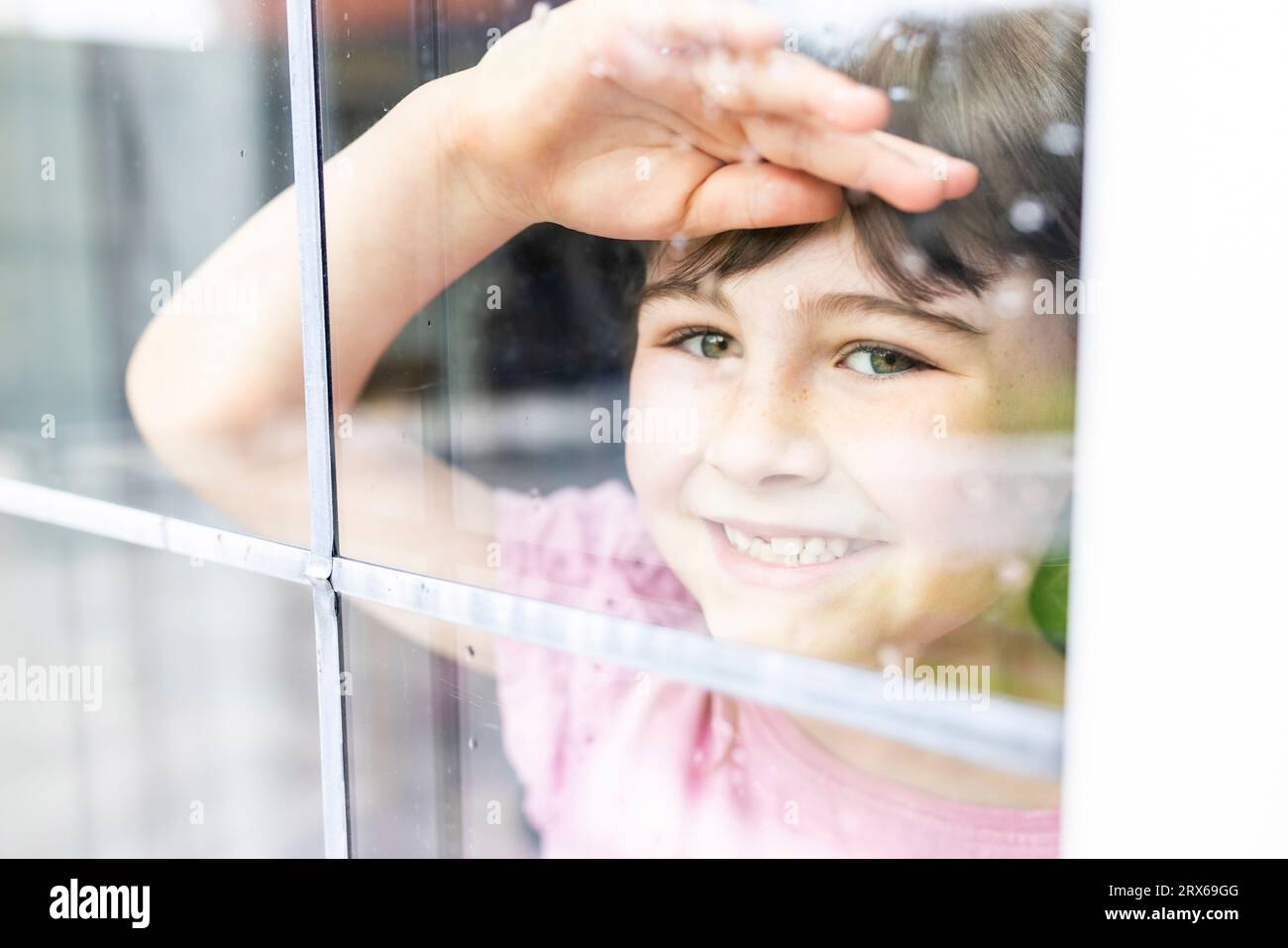 Fille souriante regardant par la fenêtre Banque D'Images