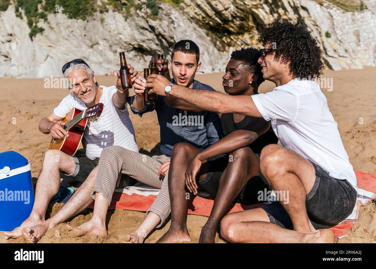 Amis multiethniques grillant des bouteilles de bière à la plage en vacances Banque D'Images