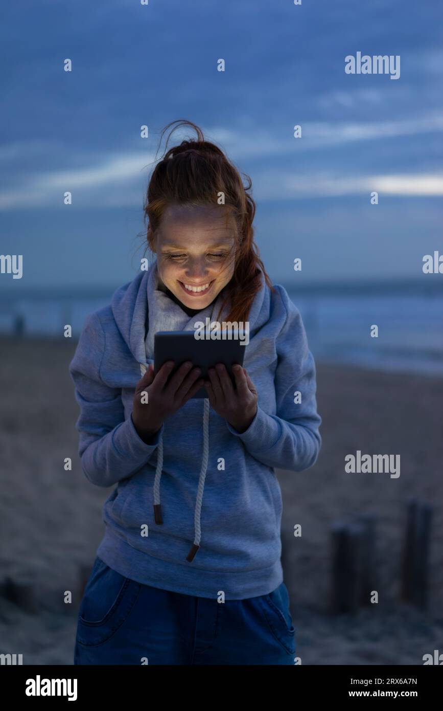 Femme souriante à l'aide d'une tablette PC à la plage en vacances Banque D'Images