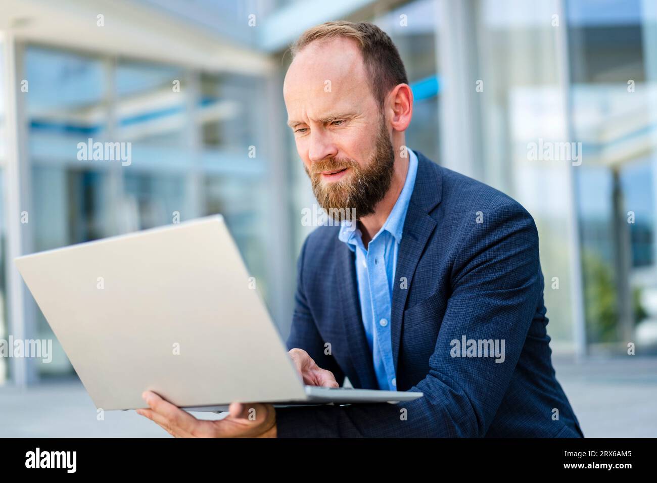 Homme d'affaires assis en face de l'immeuble de bureaux en utilisant un ordinateur portable Banque D'Images