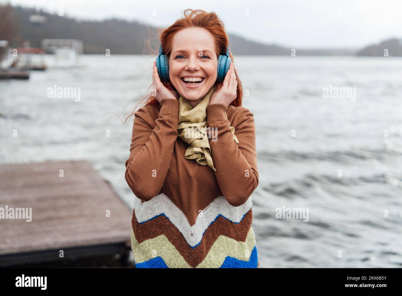 Femme joyeuse écoutant de la musique à travers des écouteurs sans fil par le lac Banque D'Images