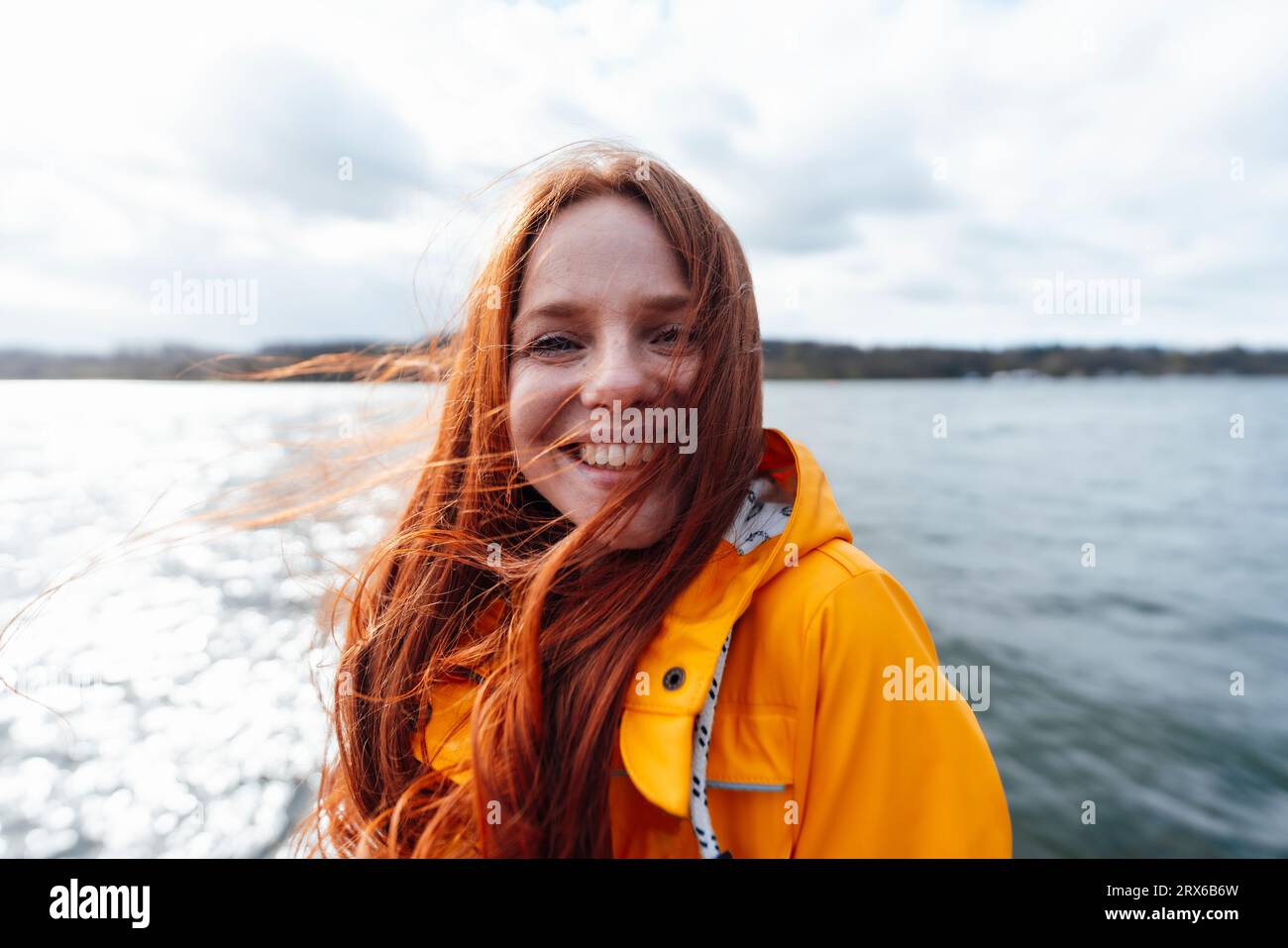Femme rousse souriante avec de longs cheveux devant le lac Banque D'Images