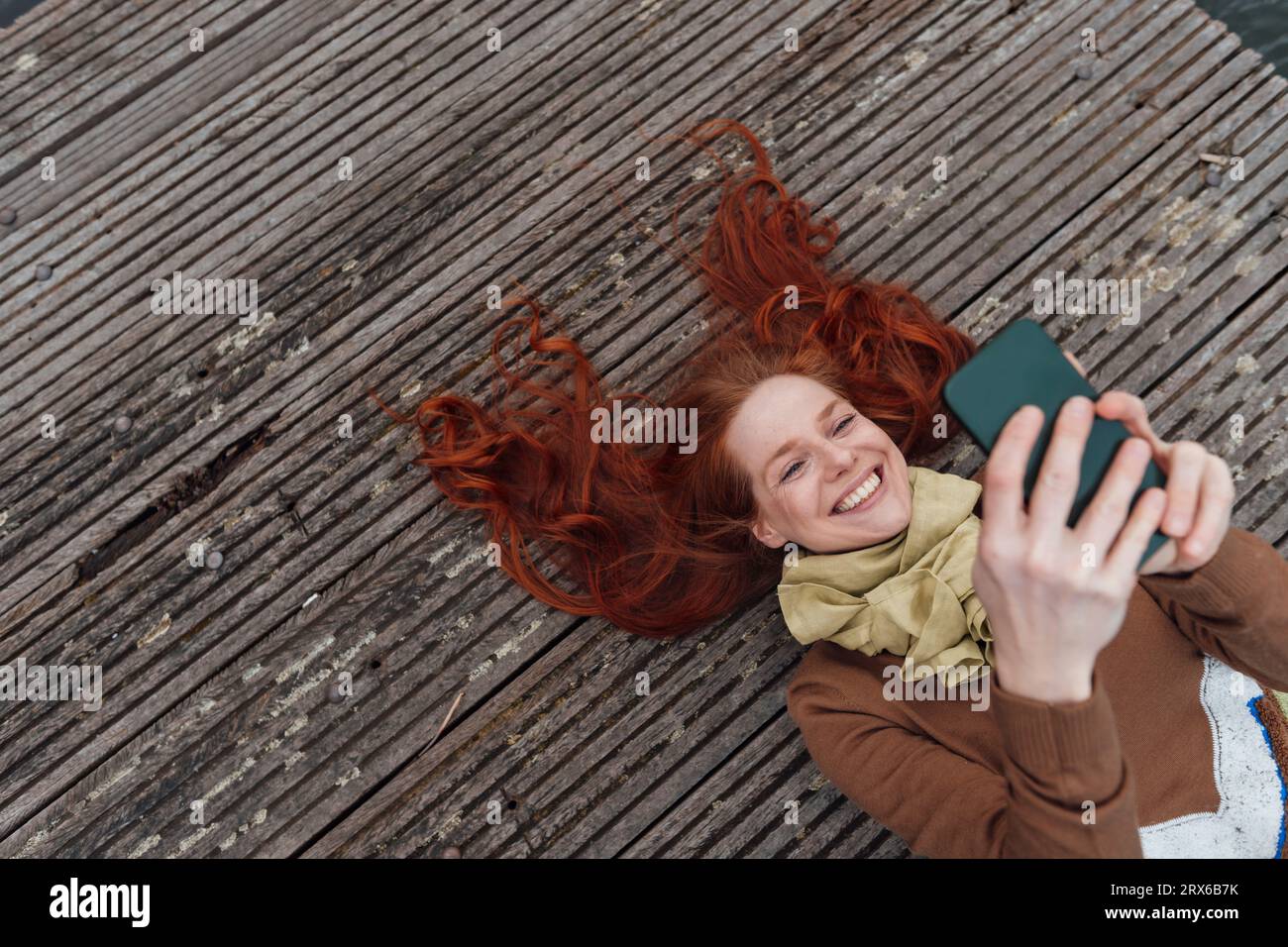Heureuse femme rousse à l'aide d'un téléphone portable couché sur la jetée Banque D'Images