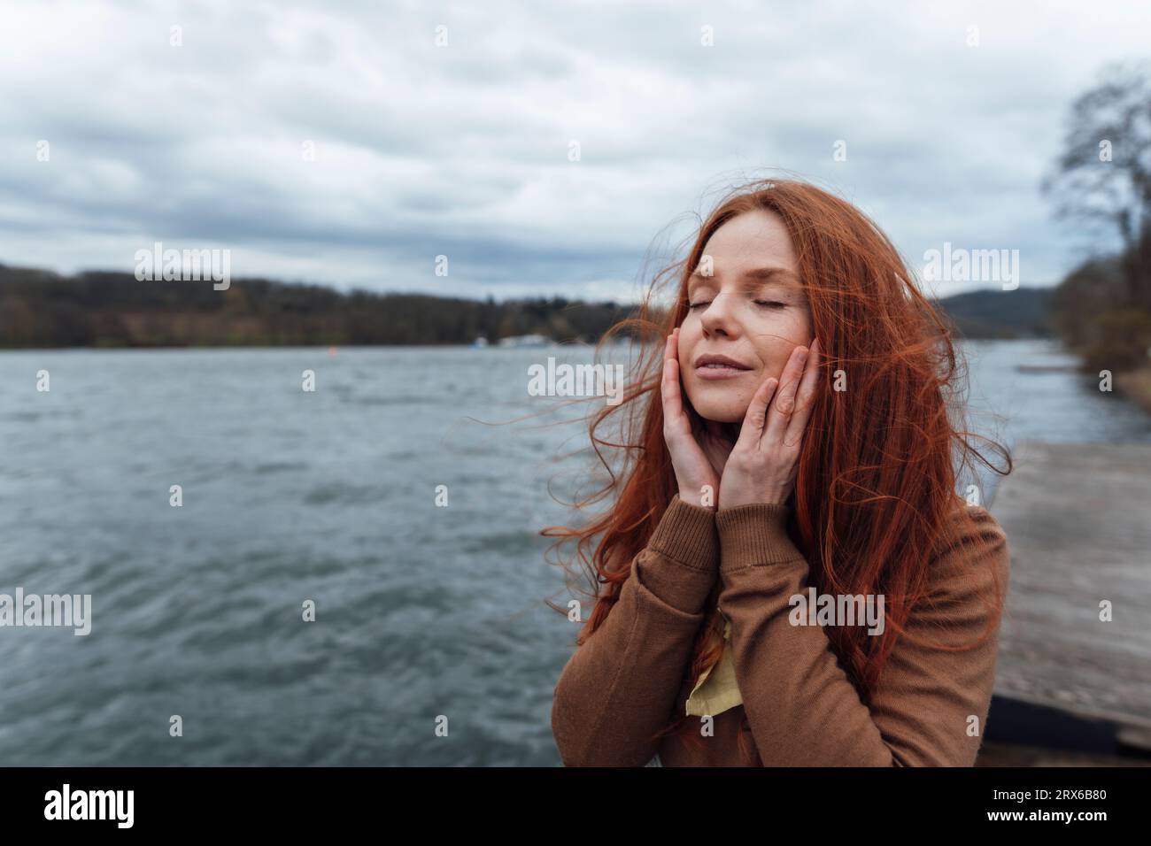 Femme touchant le visage avec les yeux fermés devant le lac Banque D'Images
