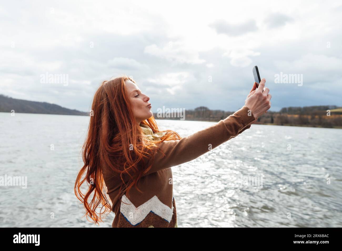 Redhead femme prenant selfie sur téléphone intelligent par le lac Banque D'Images