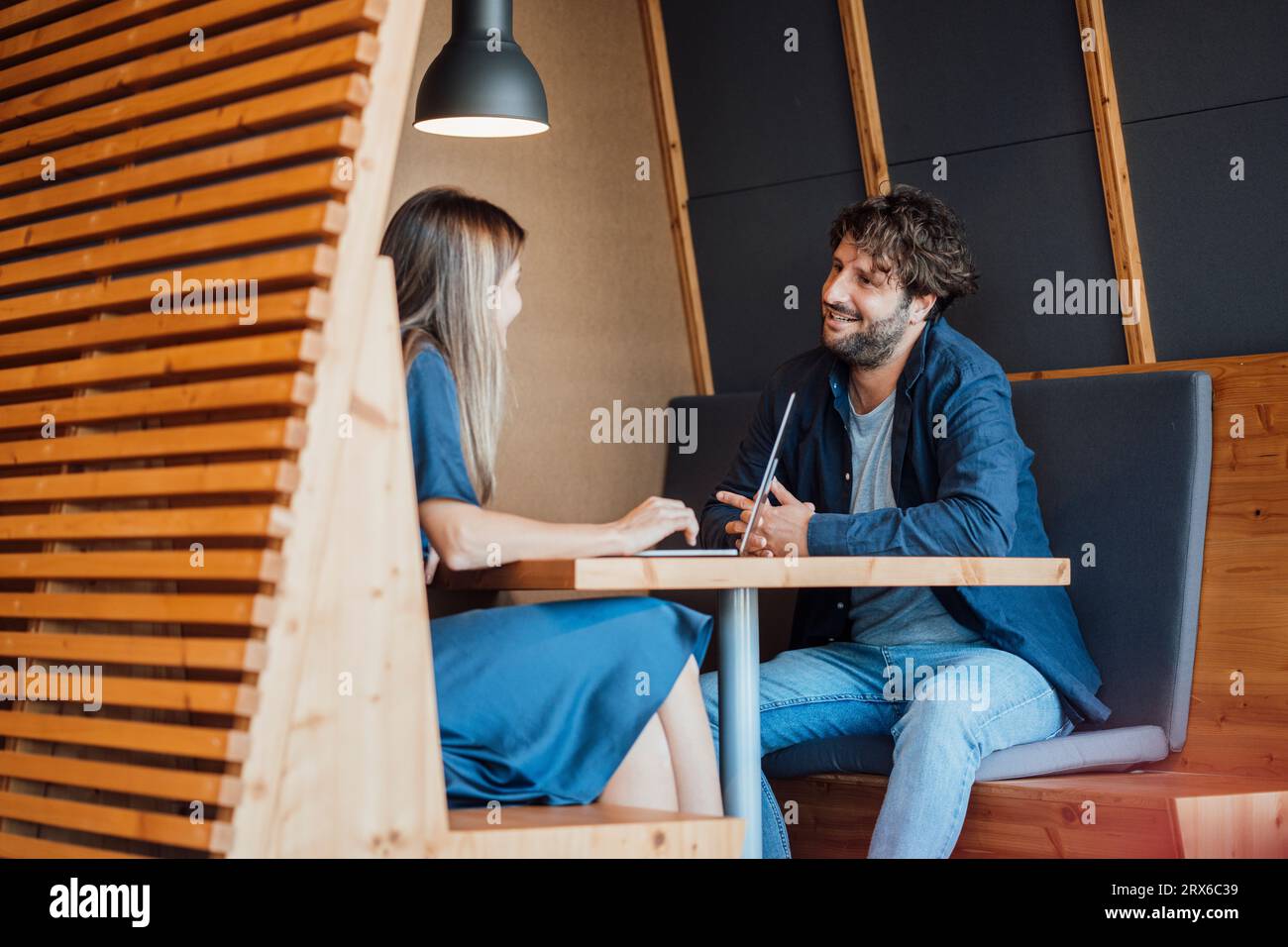 Souriant les gens d'affaires assis avec un ordinateur portable et parlant dans le bureau Banque D'Images