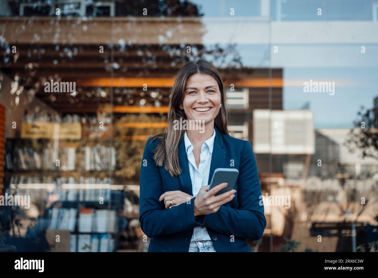 Femme d'affaires souriante tenant le téléphone intelligent devant le verre Banque D'Images