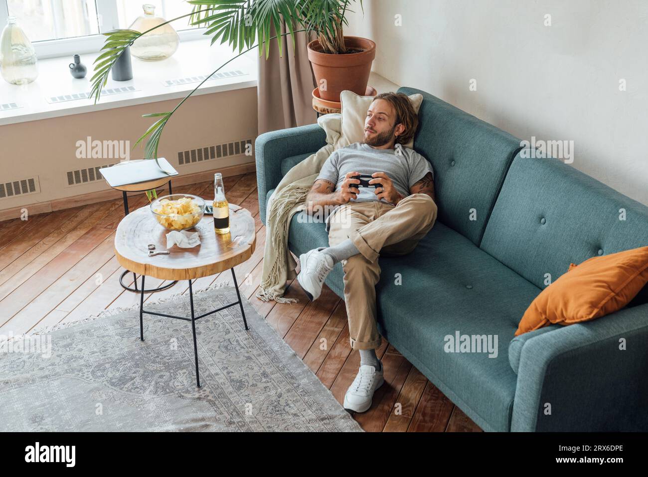 Homme avec contrôleur de jeu couché sur le canapé à la maison Banque D'Images