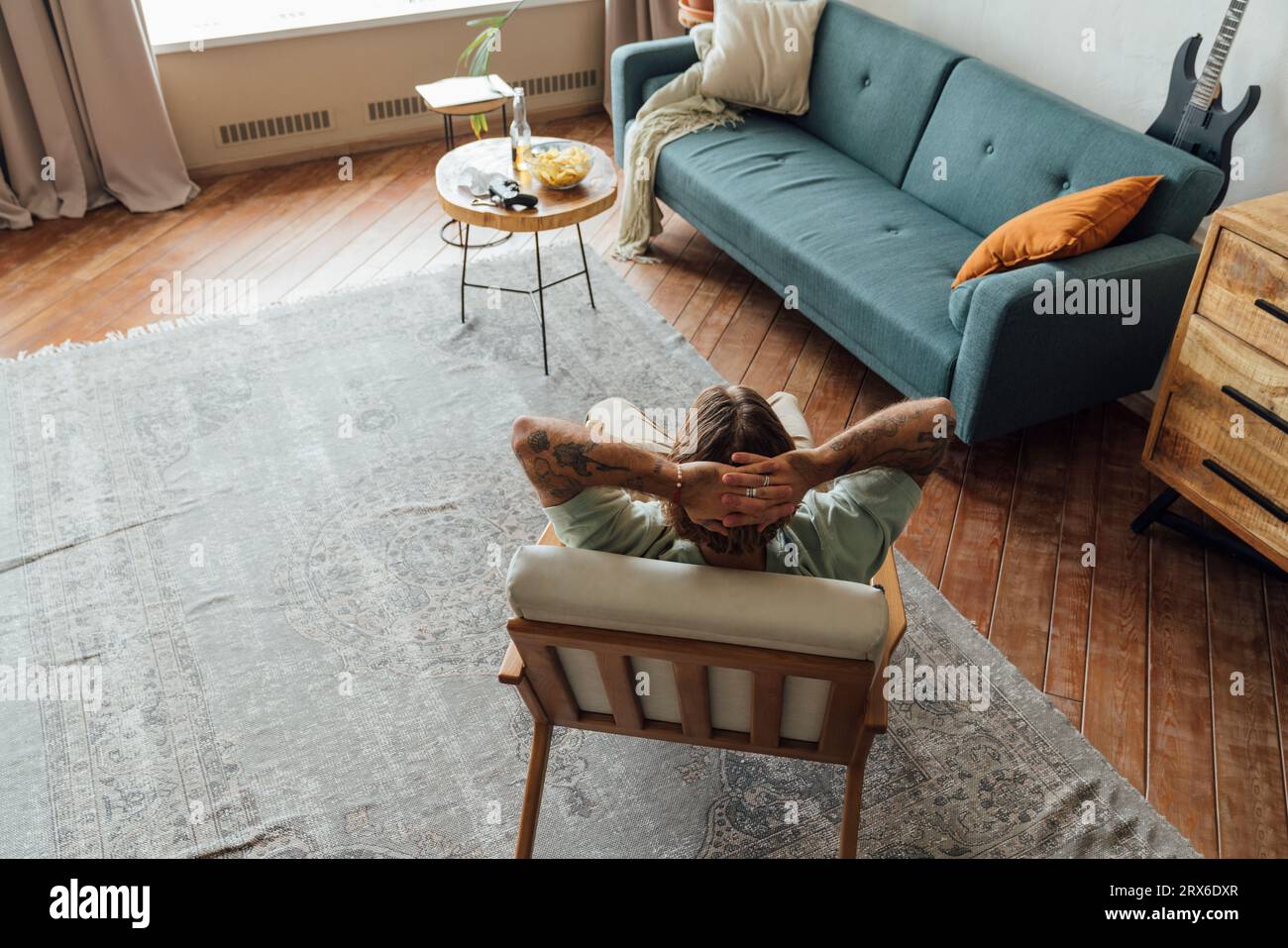 Homme avec les mains derrière la tête se relaxant sur le fauteuil dans le salon à la maison Banque D'Images