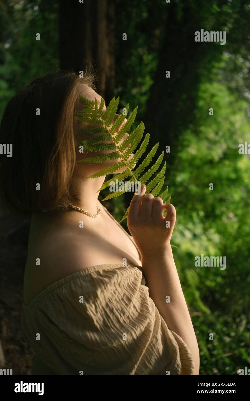 Jeune femme couvrant le visage avec la feuille de fougère dans le jardin Banque D'Images