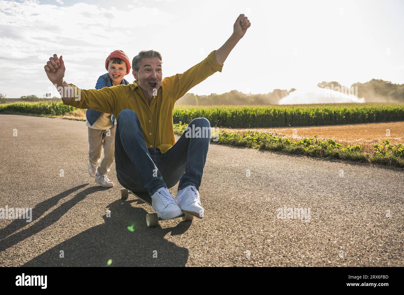 Homme joyeux se faisant pousser par petit-fils sur skateboard Banque D'Images