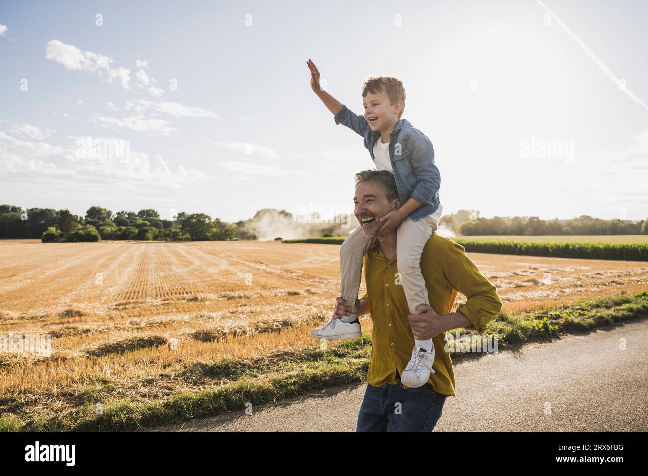 Homme appréciant porter petit-fils sur les épaules au jour ensoleillé Banque D'Images