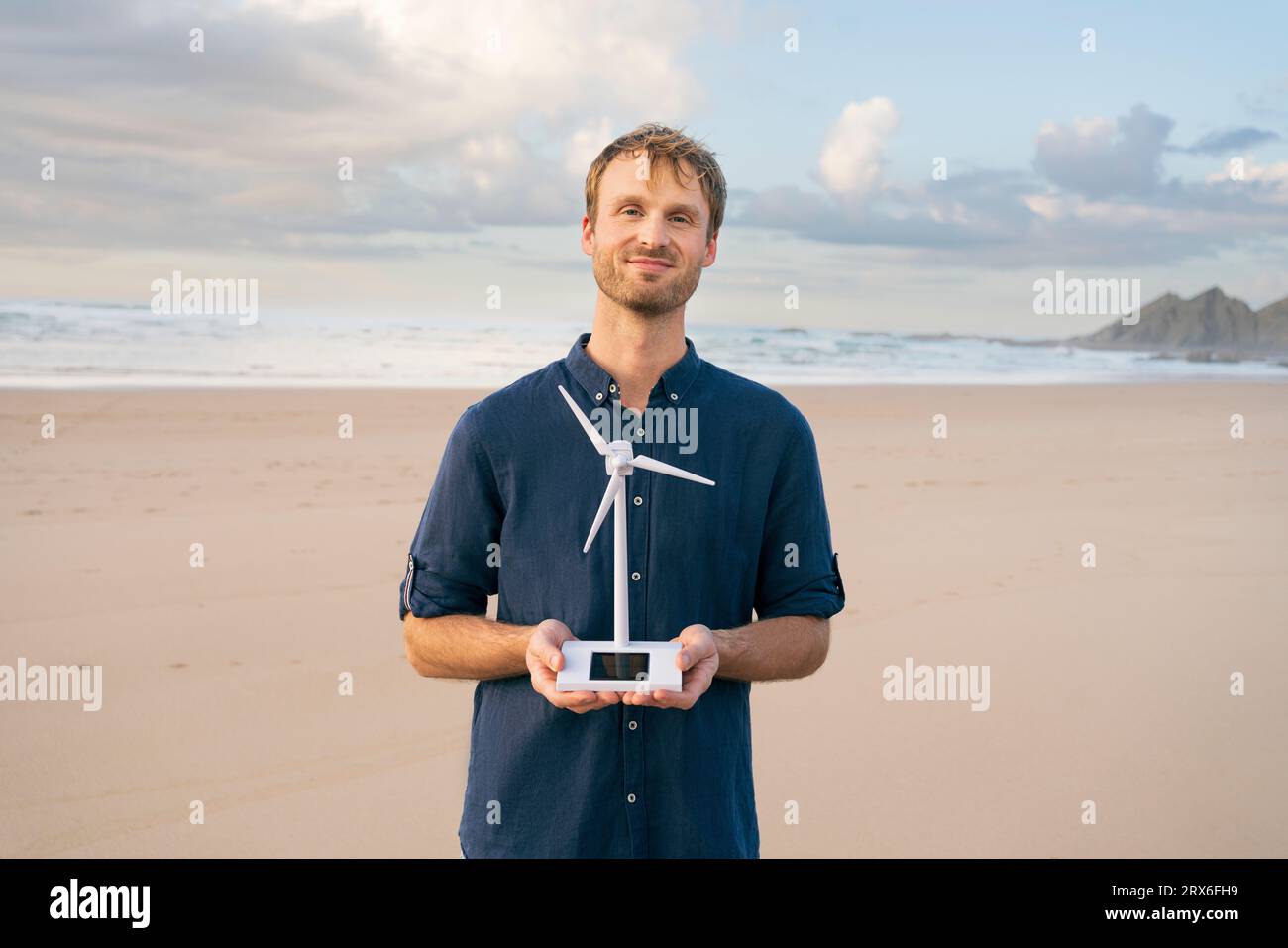 Homme souriant tenant le modèle d'éolienne à la plage Banque D'Images