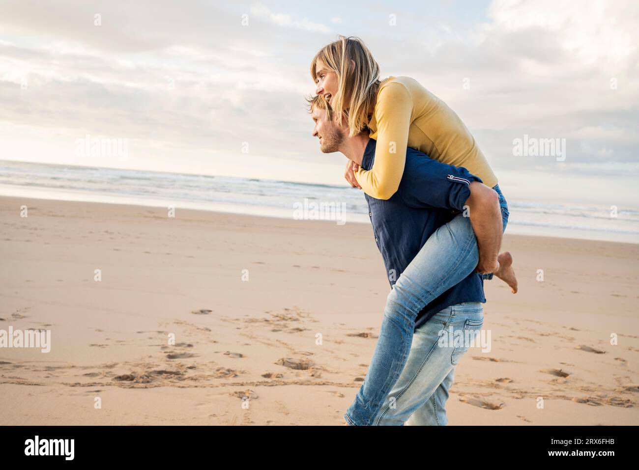 Homme souriant donnant tour de piggyback à la femme à la plage Banque D'Images