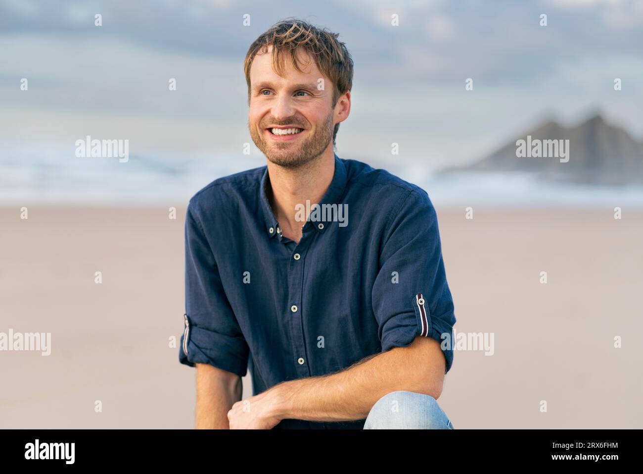 Homme souriant accroupi à la plage Banque D'Images