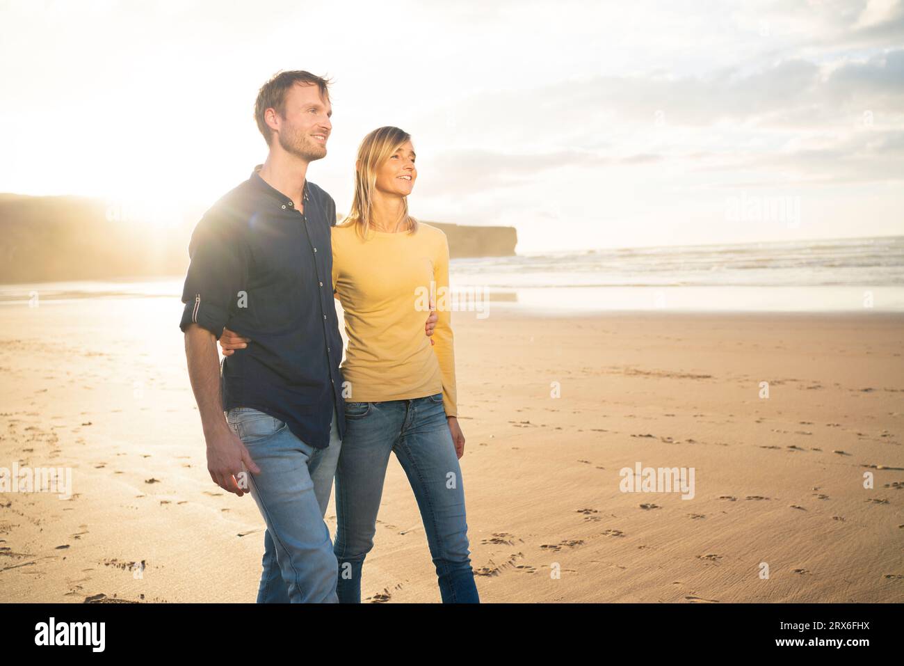 Couple souriant marchant sur le sable au coucher du soleil Banque D'Images