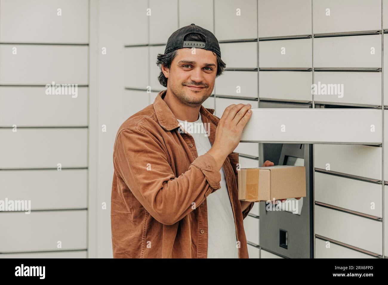 Homme heureux portant une chemise brune tenant le paquet de livraison près du casier Banque D'Images