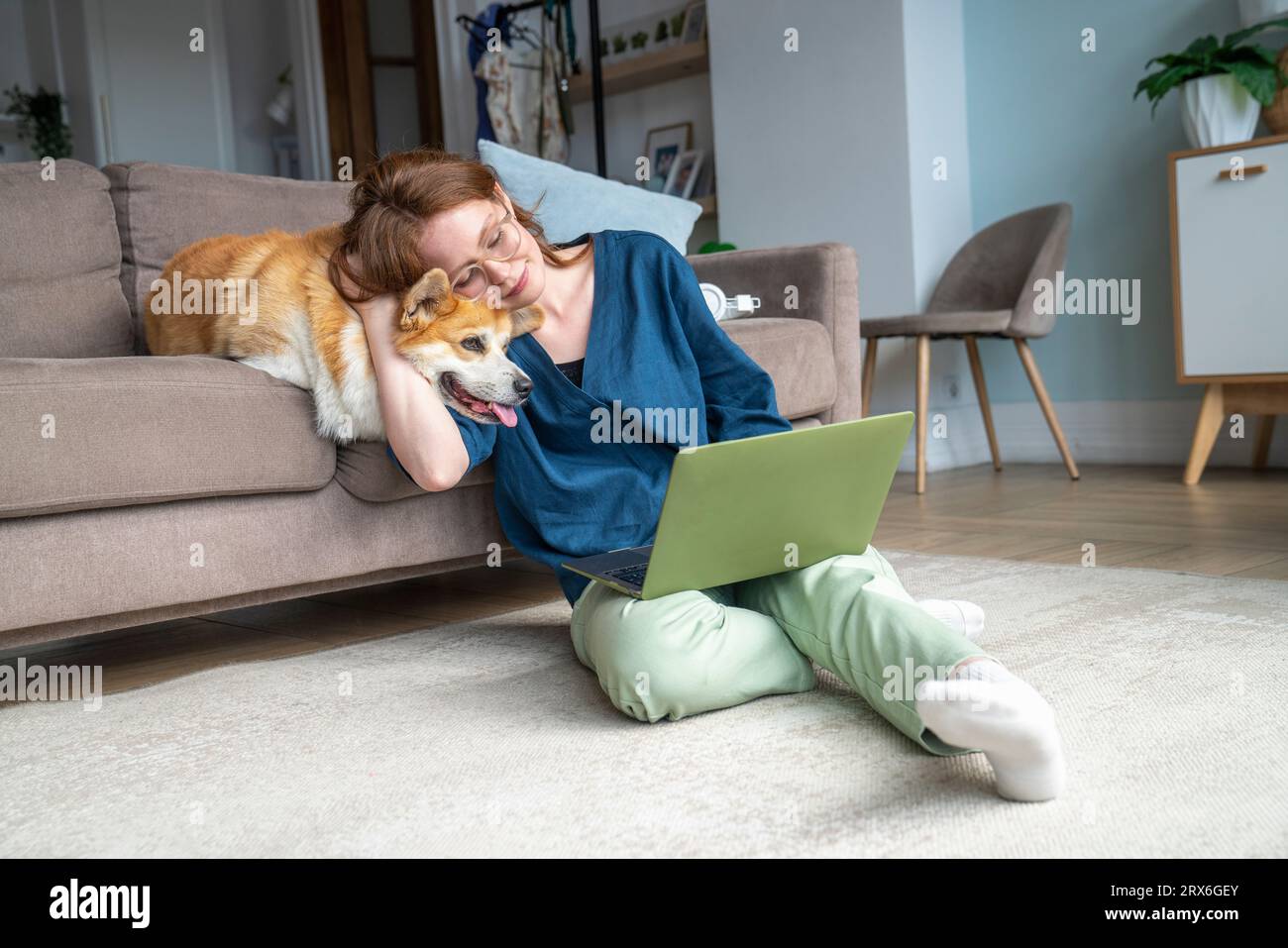 Femme utilisant un ordinateur portable et câlinant chien dans le salon Banque D'Images
