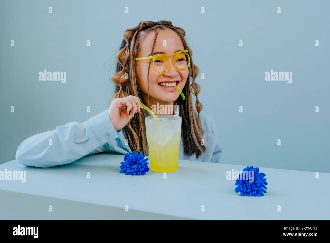 Jeune femme souriante buvant avec de la paille comme du verre à table dans le studio Banque D'Images