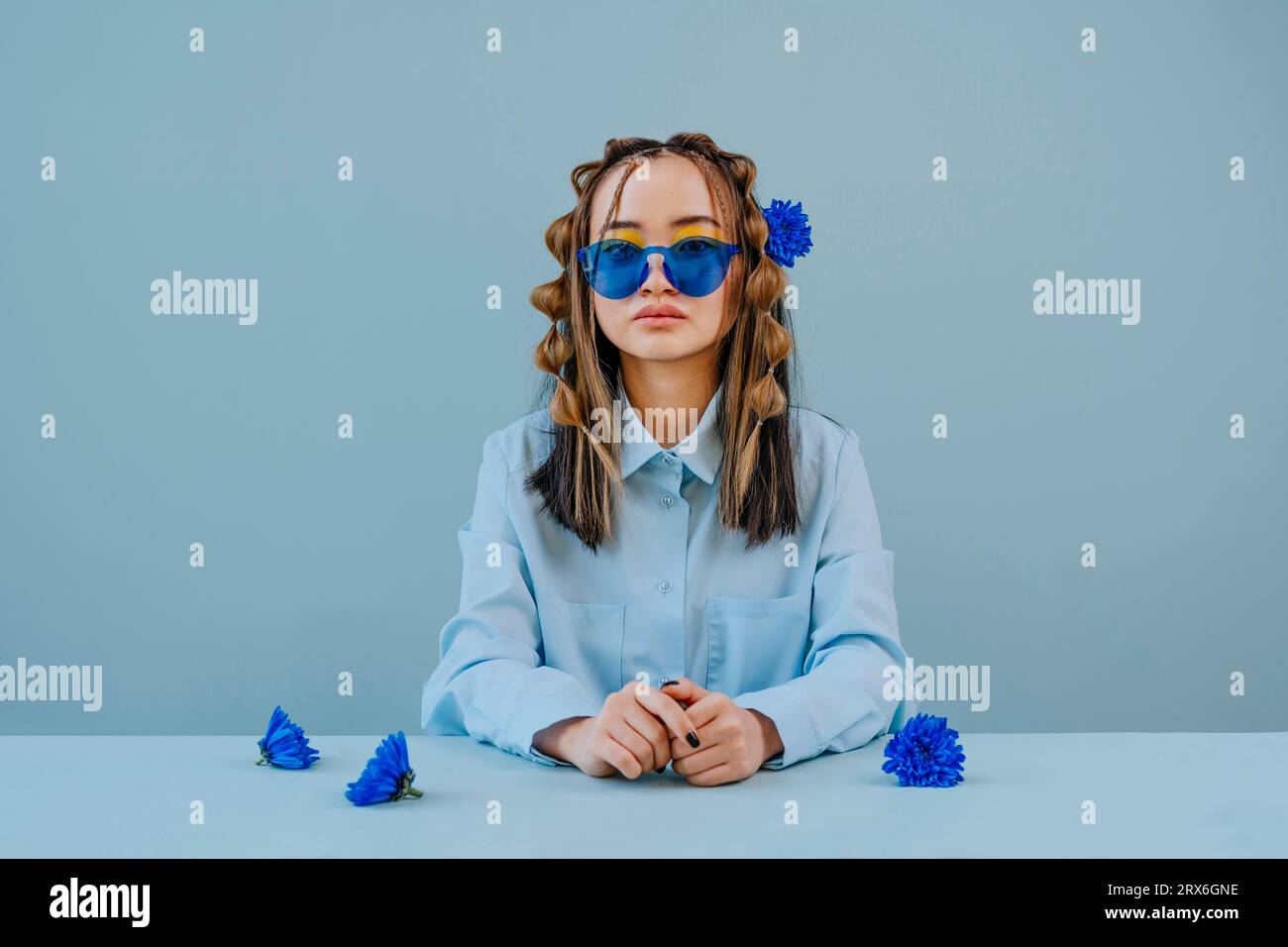 Jeune femme portant des lunettes bleues assise à table avec des fleurs sur fond bleu Banque D'Images