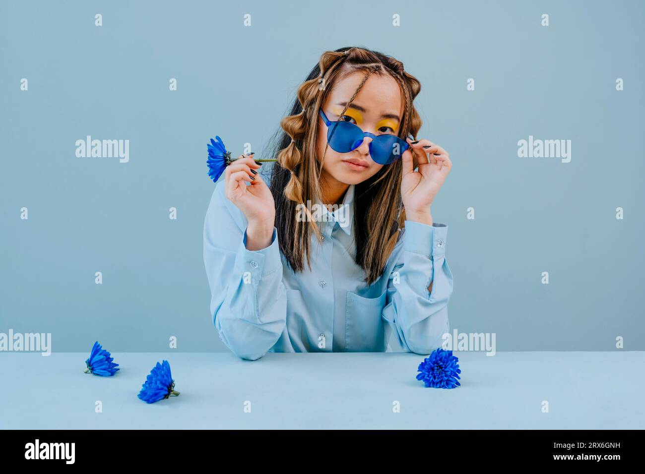 Femme portant des lunettes bleues avec des fleurs bleues sur la table en studio Banque D'Images