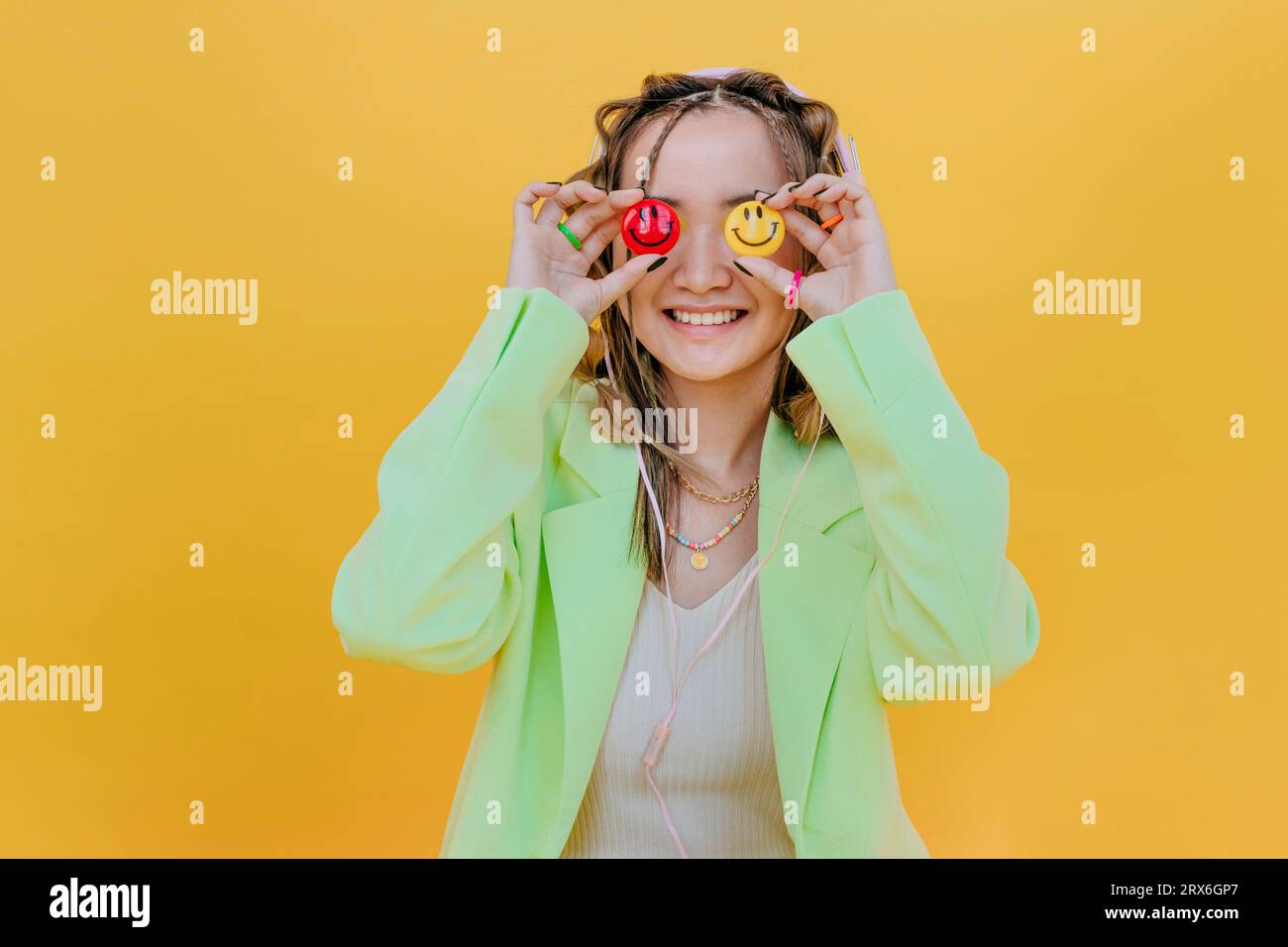 Femme souriante couvrant les yeux avec des smileys sur fond jaune Banque D'Images Femme souriante couvrant les yeux avec des smileys sur fond jaune Banque D'Images