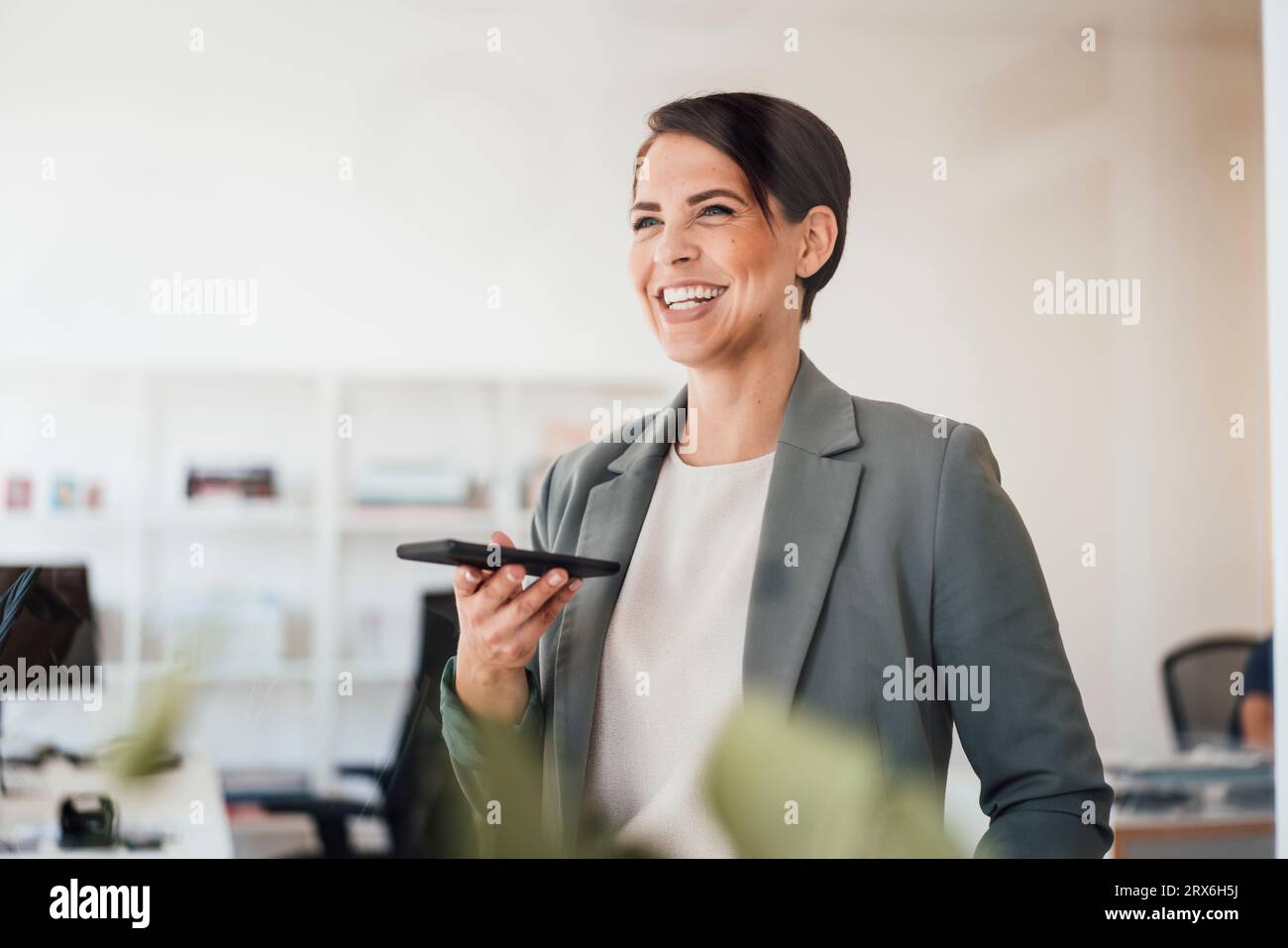 Femme d'affaires heureuse avec téléphone intelligent sur le lieu de travail Banque D'Images