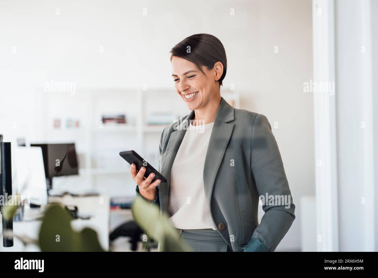 Femme d'affaires souriante utilisant un smartphone au bureau Banque D'Images