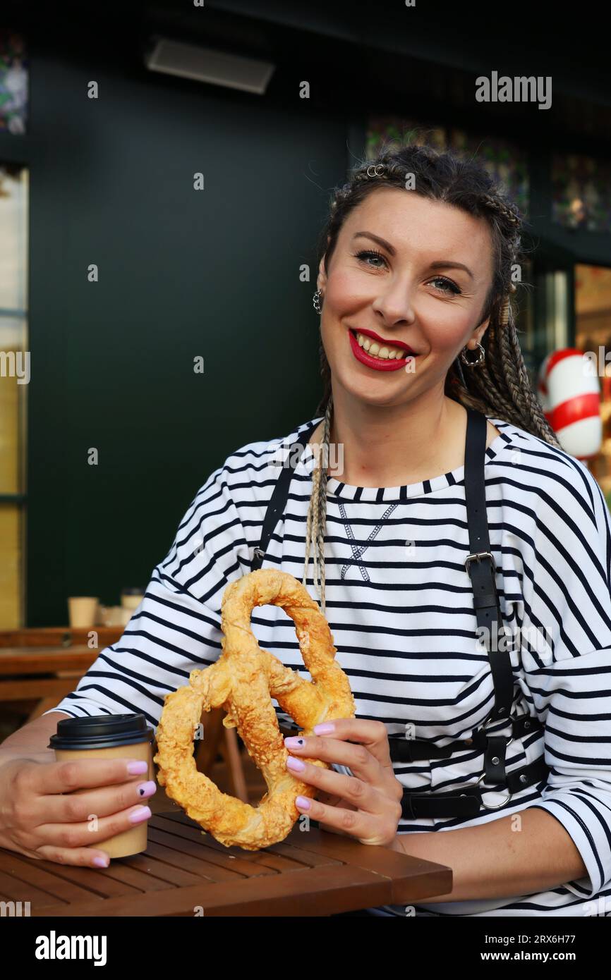 Une jeune femme avec une coiffure élégante tient un bagel dans ses mains, apporte un bagel à son œil avec une expression ludique sur son visage. Gros plan portrait Banque D'Images Une jeune femme avec une coiffure élégante tient un bagel dans ses mains, apporte un bagel à son œil avec une expression ludique sur son visage. Gros plan portrait Banque D'Images