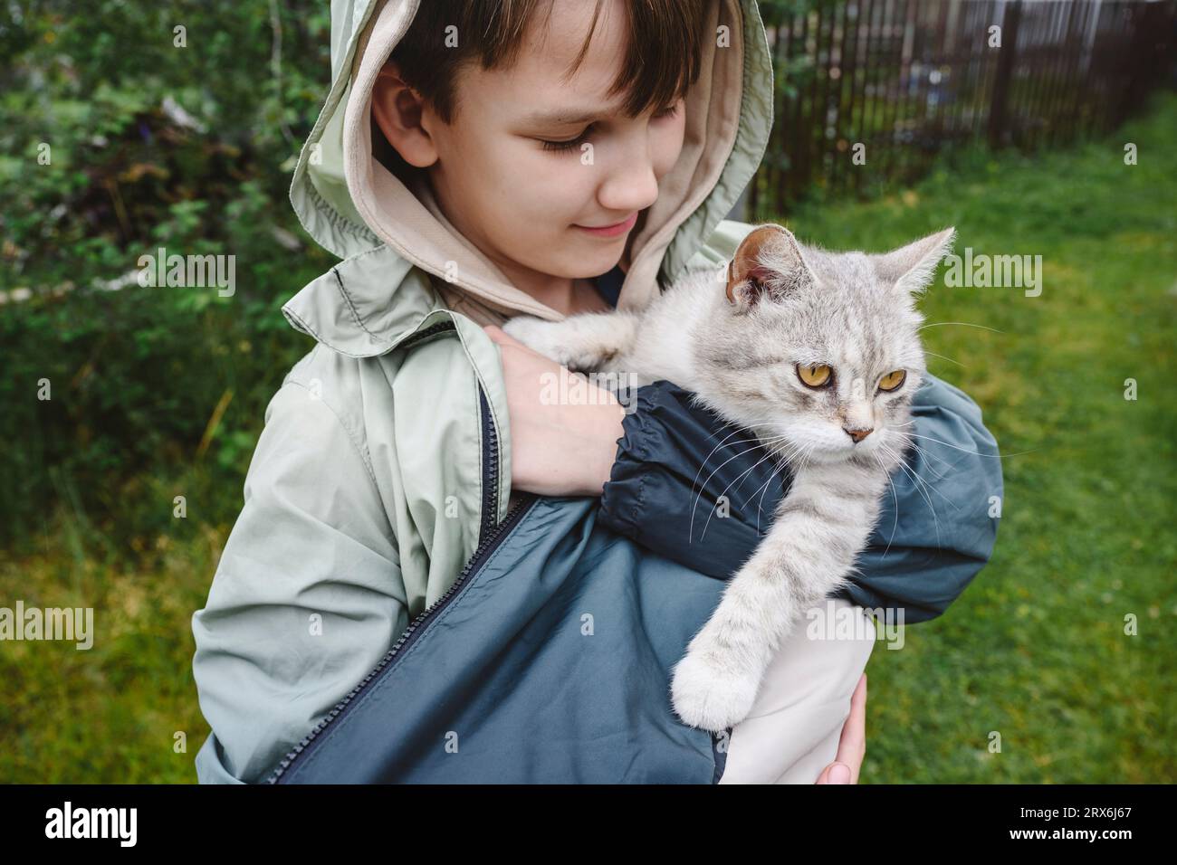 Garçon souriant portant une veste portant un chat dans le jardin Banque D'Images