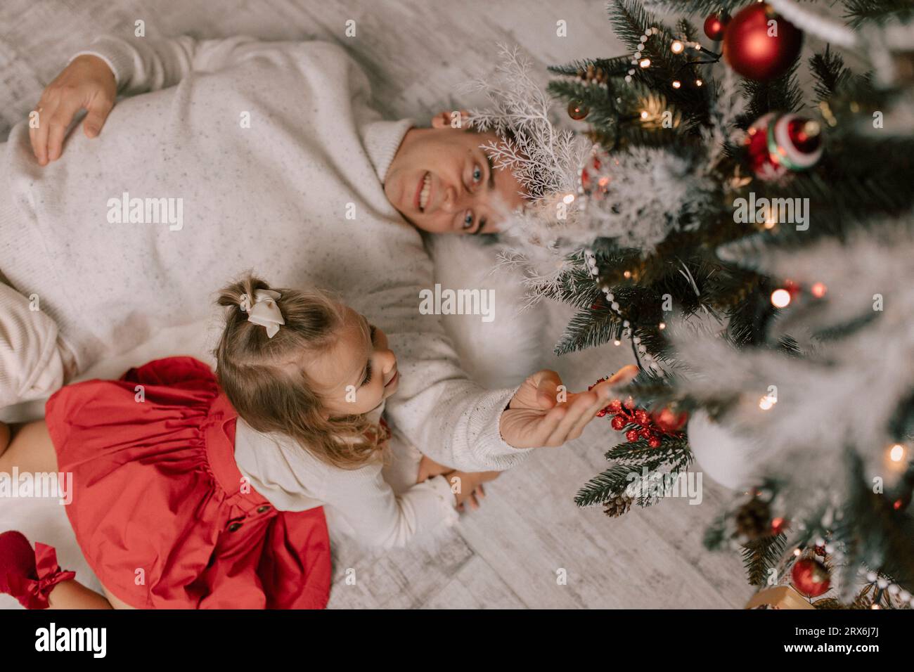 Père et fille ludiques couchés sur le sol et touchant le sapin de noël Banque D'Images