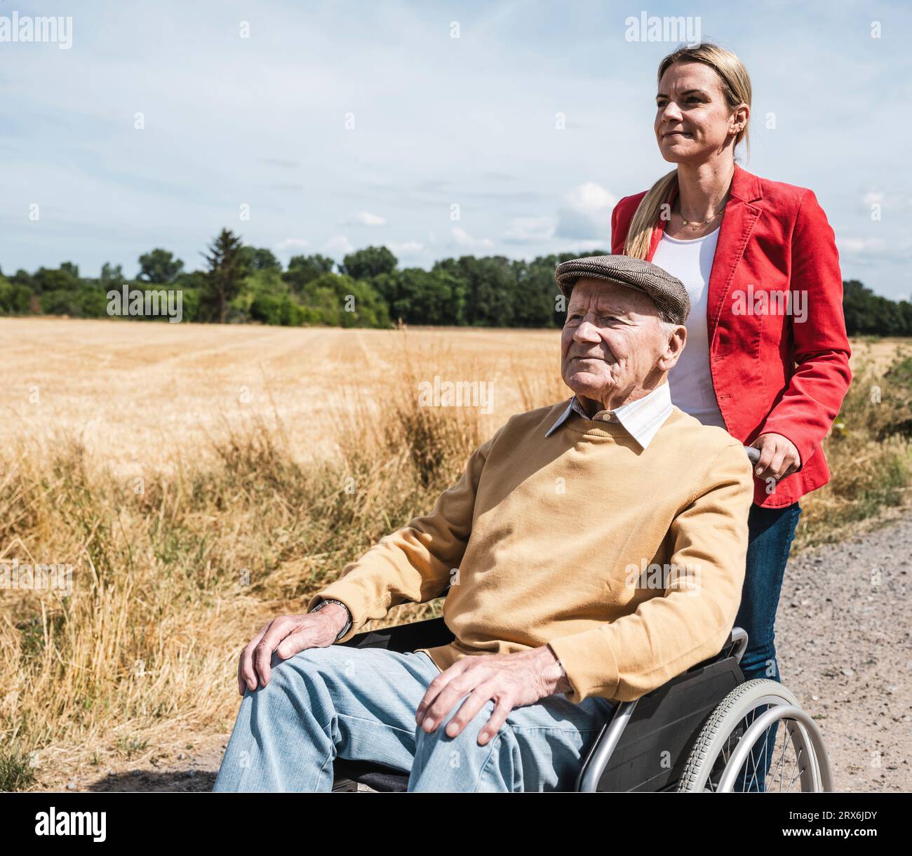 Femme poussant l'homme âgé assis en fauteuil roulant à la journée ensoleillée Banque D'Images